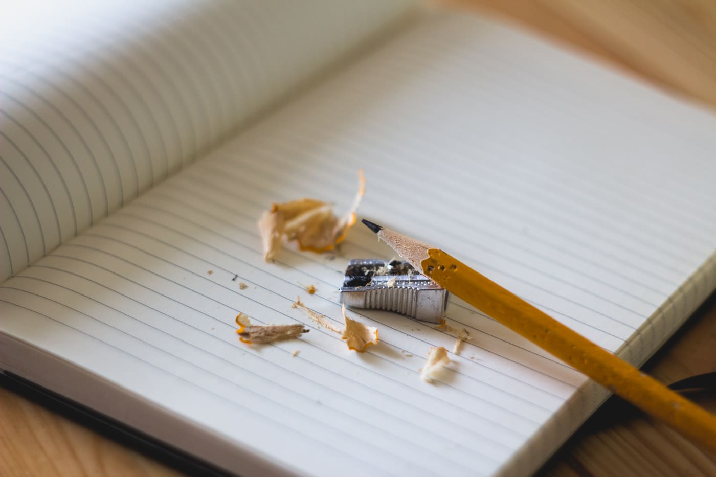 A blank notebook, pencil sharpener, and pencil shavings on a light desk.